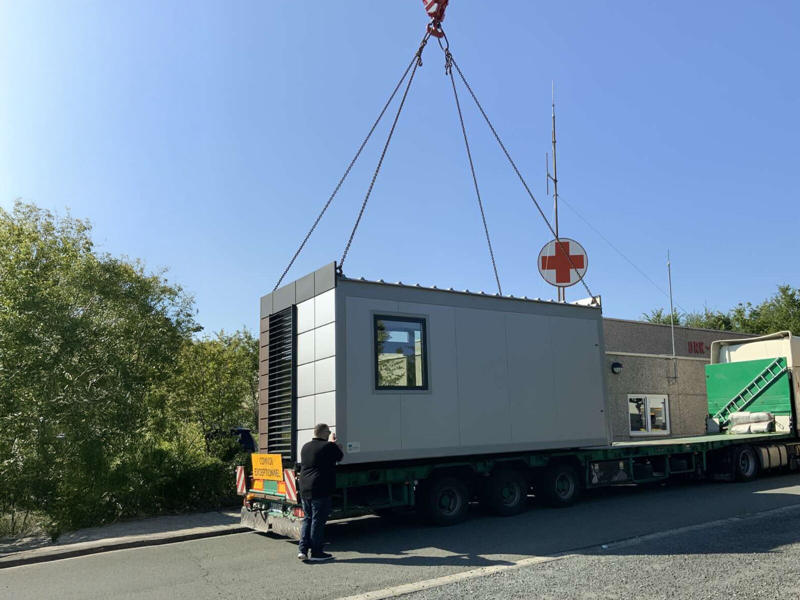 Verladung eines Containers per Kran auf einen LKW vor einer Rotkreuz-Station