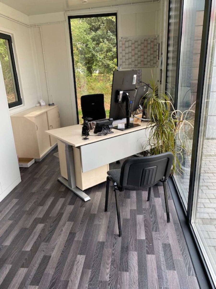 Innenansicht eines Containers mit Schreibtisch, Monitoren und großer Glasfront