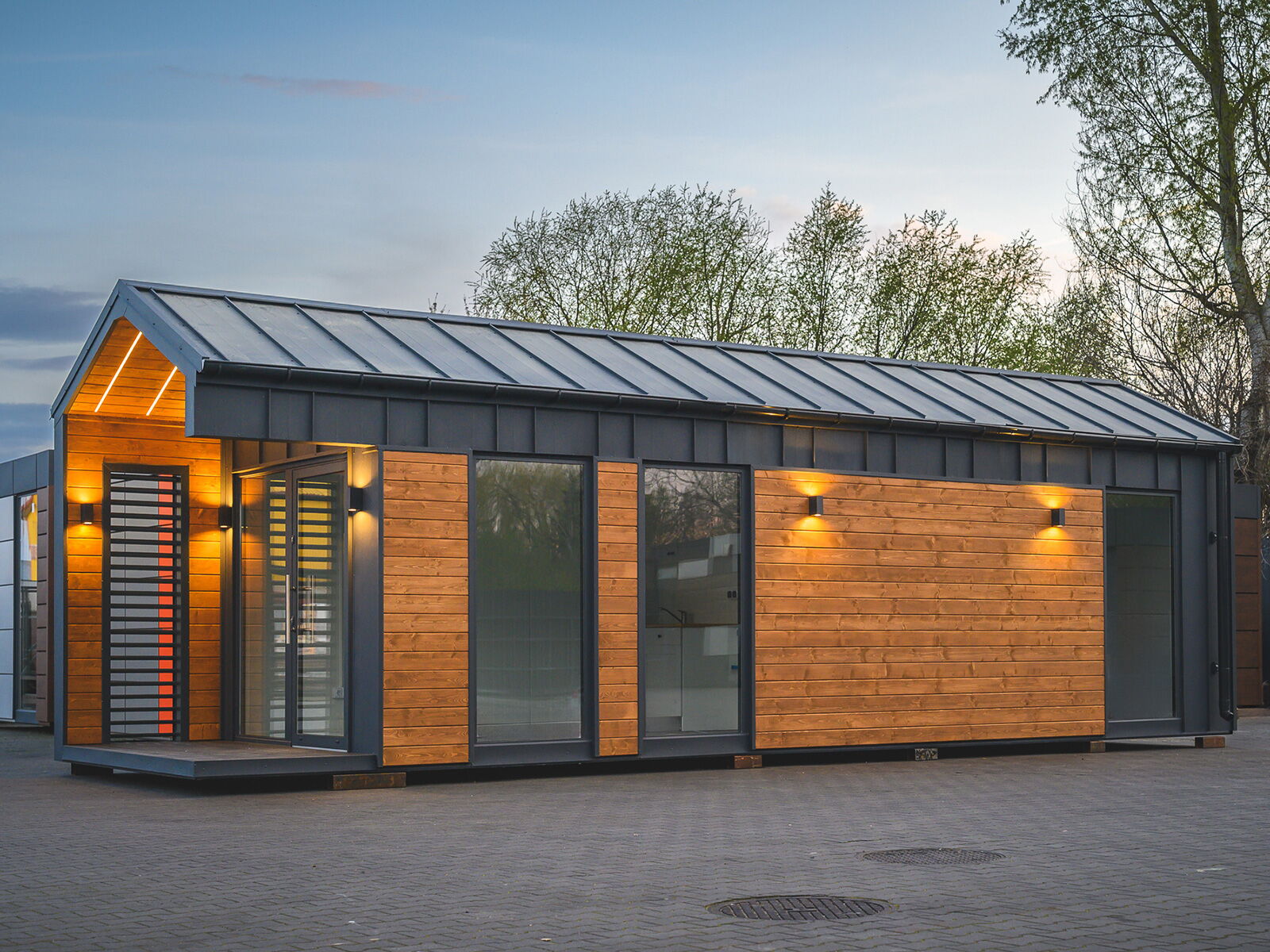 Moderner Modulcontainer mit Holzfassade und Satteldach bei Dämmerung