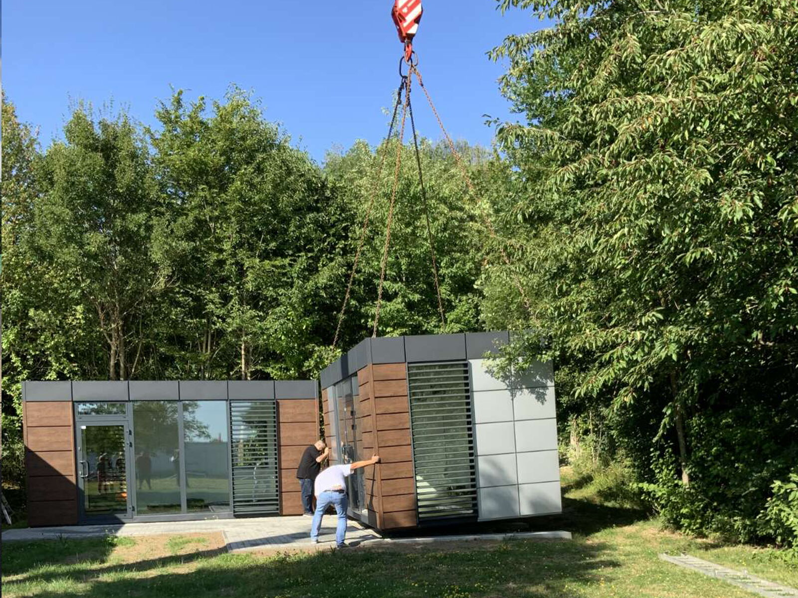 Montage eines Containers per Kran neben einem bereits installierten Modul