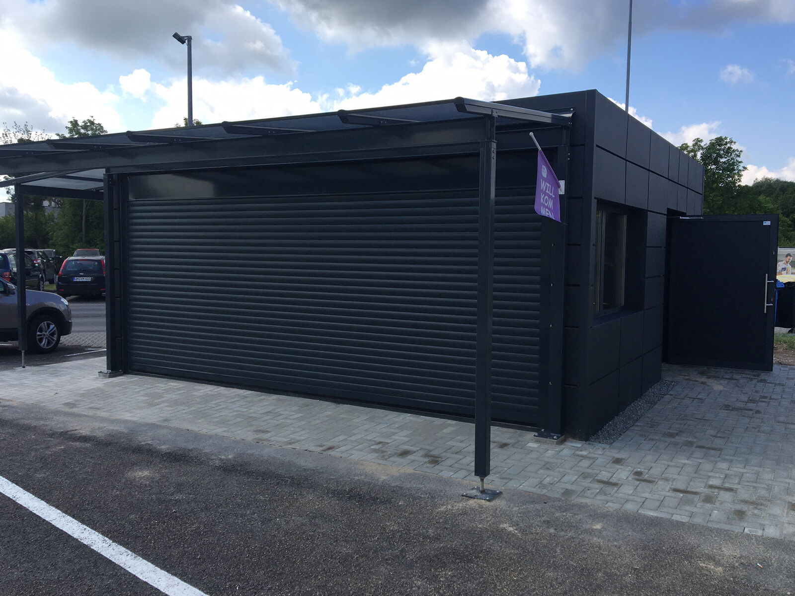 Schwarzer Container mit geschlossenem Rolltor und seitlichem Eingang