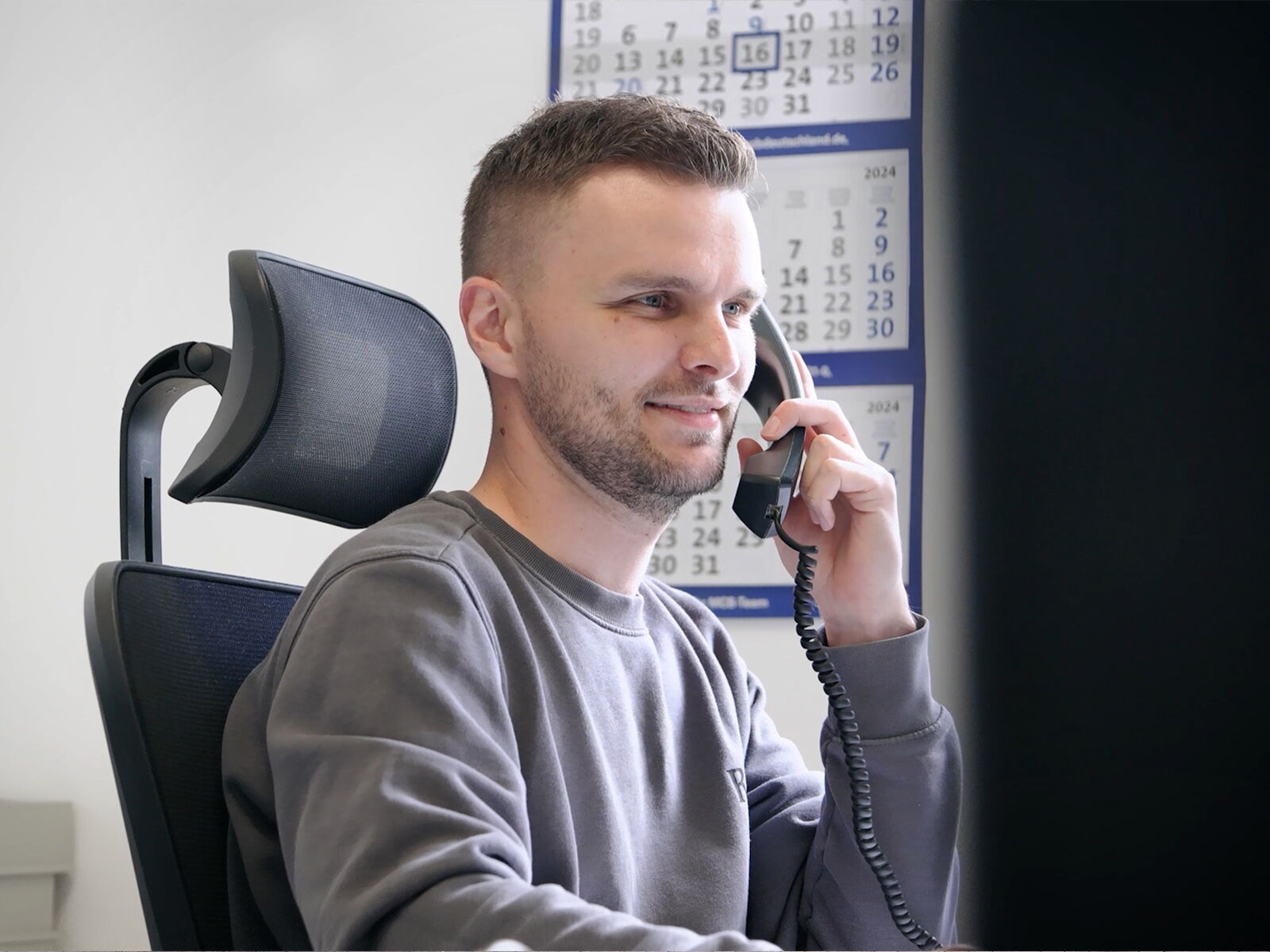 Mitarbeiter im Büro sitzt am Schreibtisch und telefoniert mit einem Festnetztelefon      