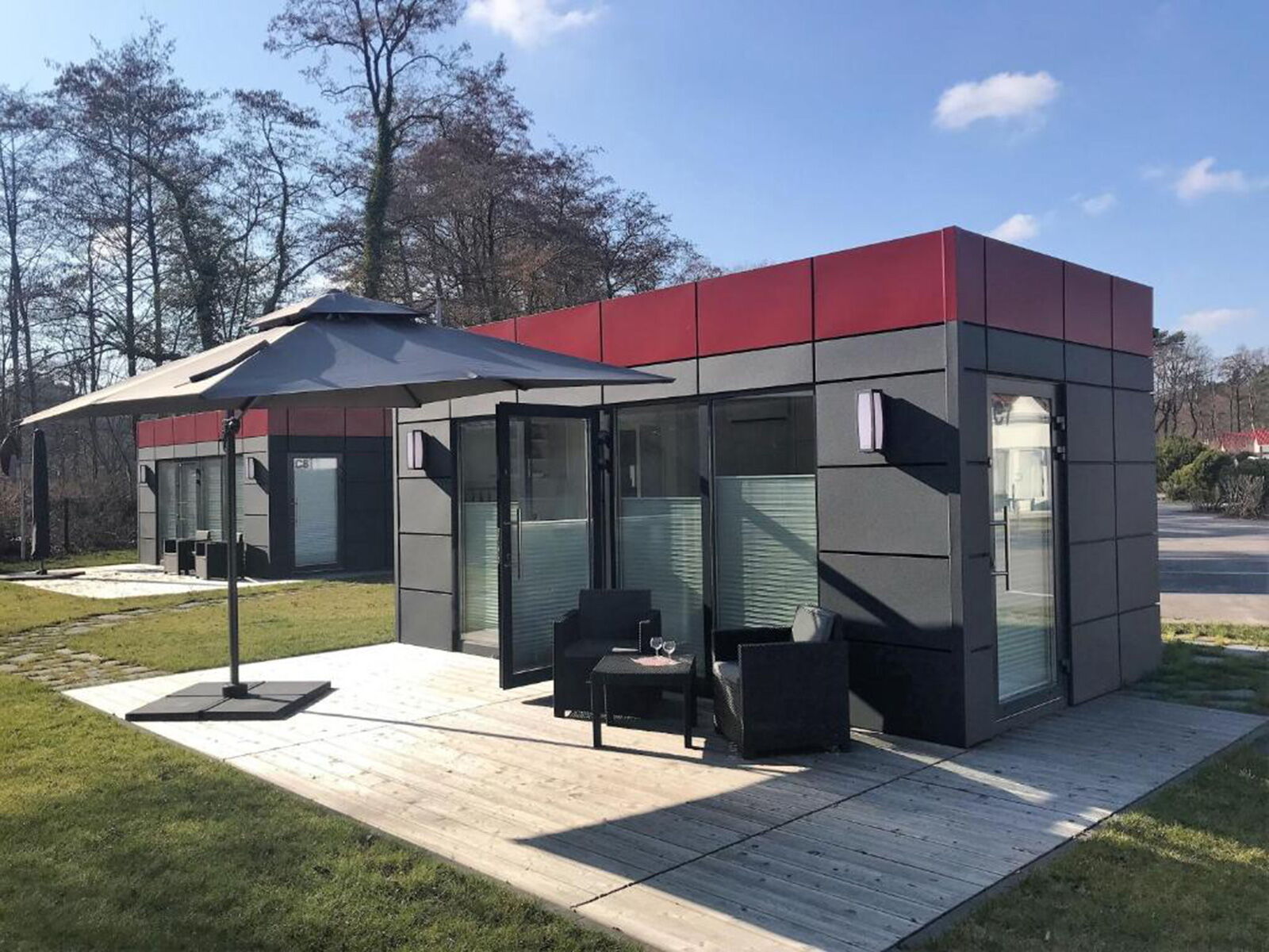 Moderner Wohncontainer mit grauer Fassade, rotem Akzent und Terrasse mit Sitzmöbeln
