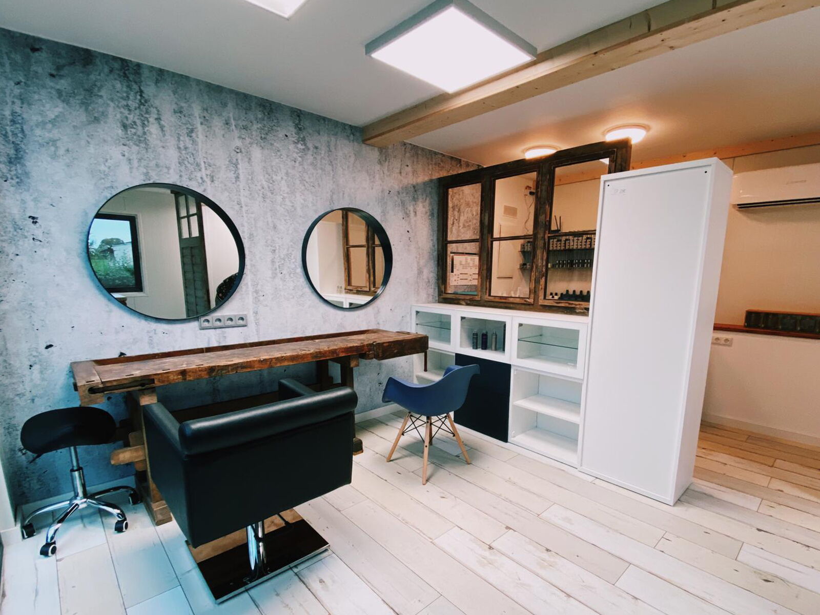 Moderner Innenraum mit Holzarbeitsplatz, runden Spiegeln, drei Stühlen und Schränken