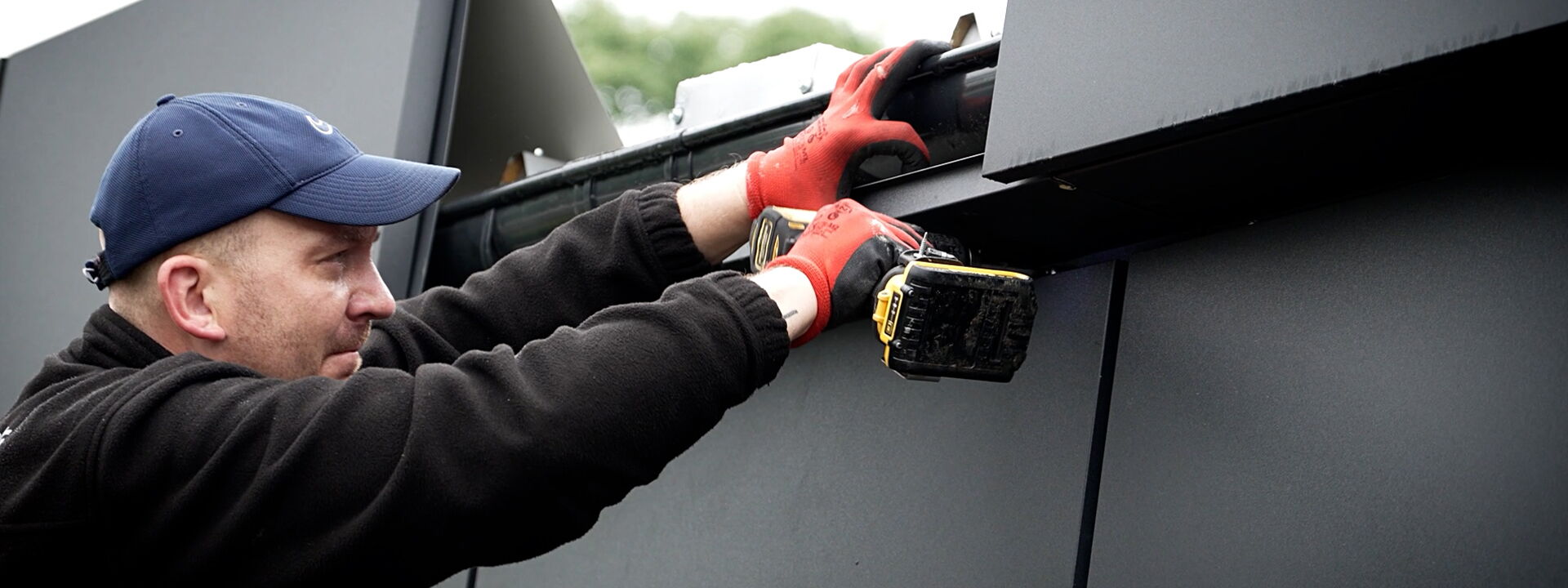 Monteur befestigt Fassadenelement an einem Container mit Akkuschrauber      