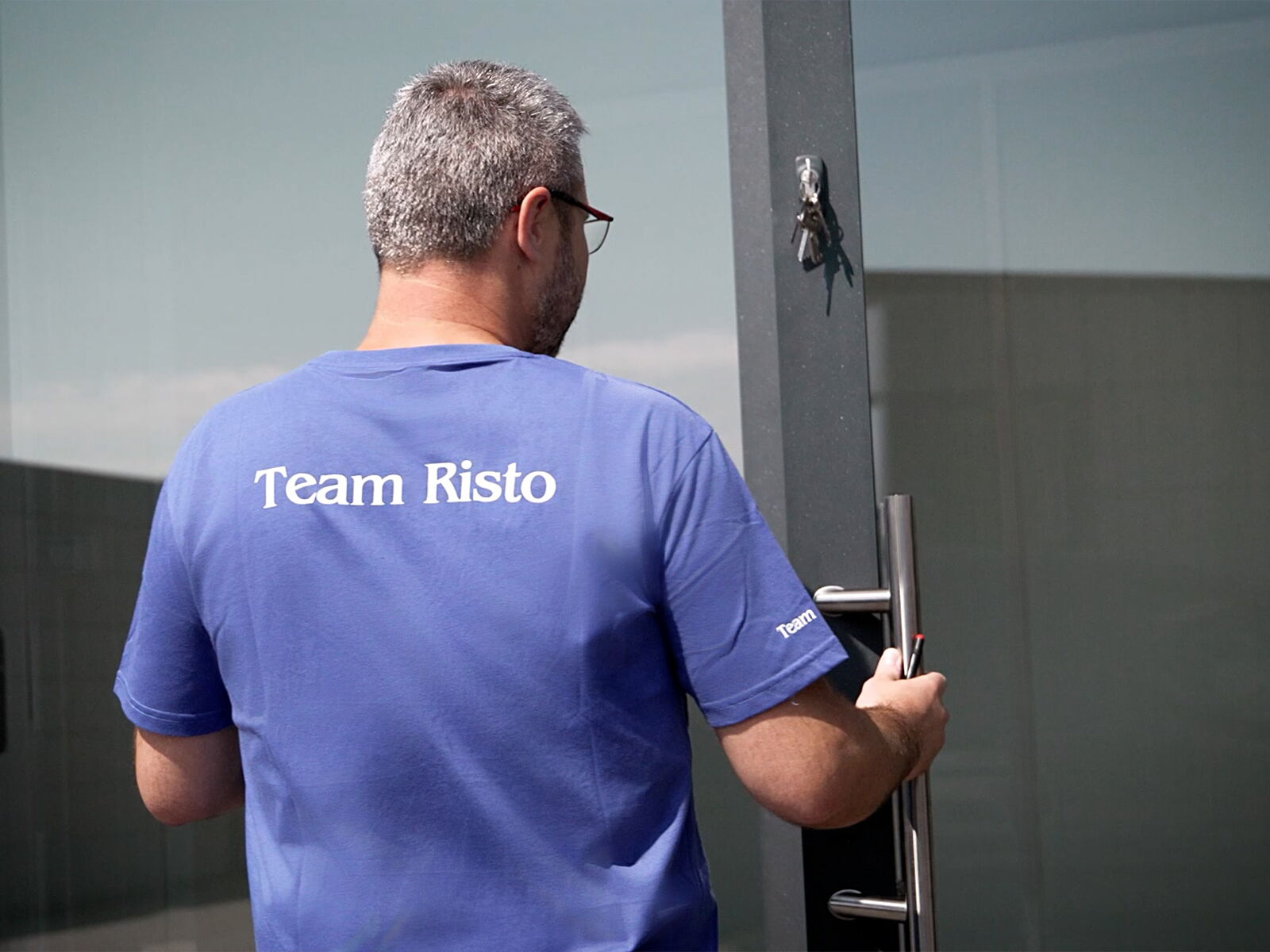 Mitarbeiter von Risto öffnet eine Glastür, T-Shirt mit Aufdruck Team Risto      