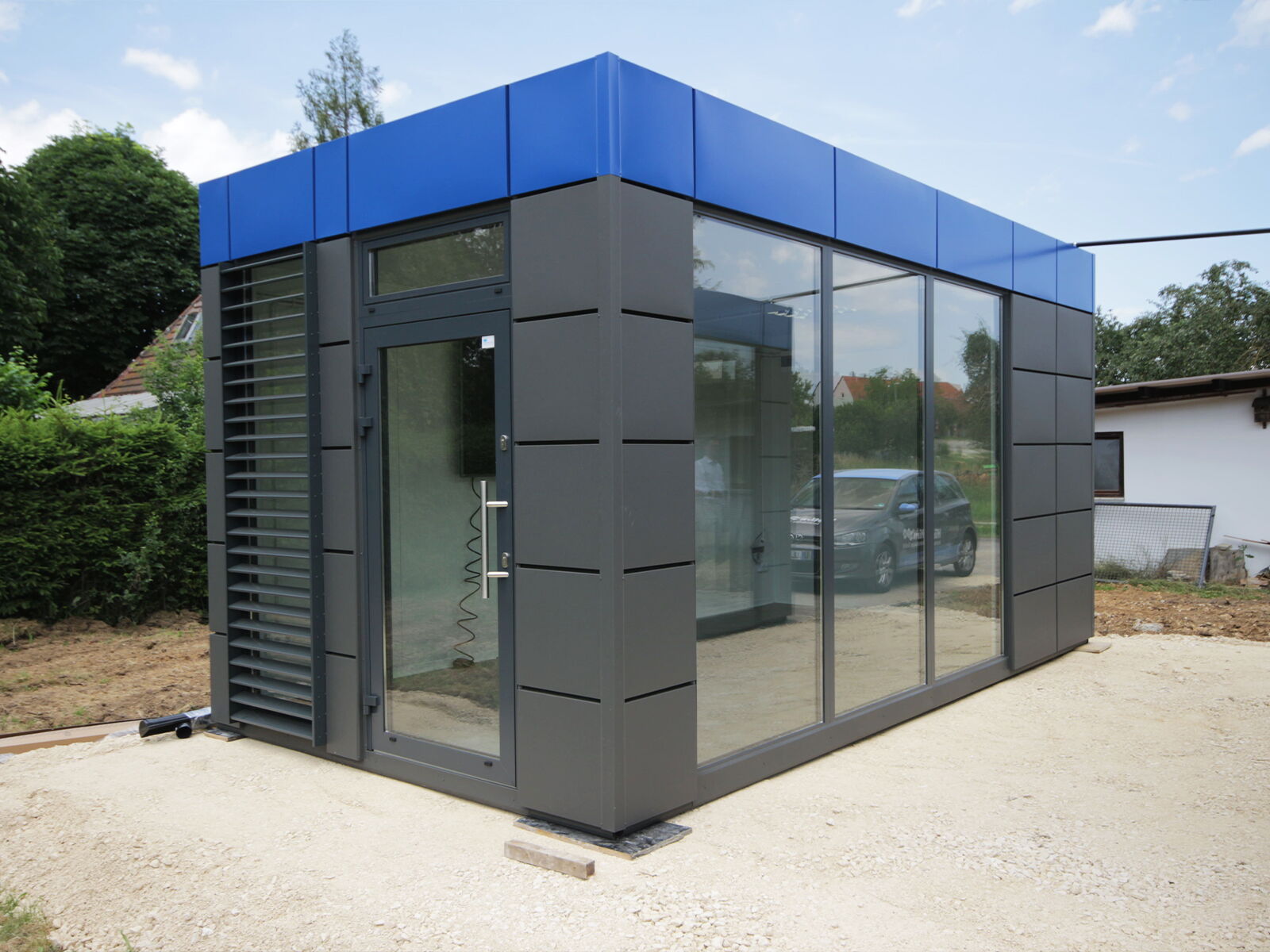 Moderner Bürocontainer mit blauer Attika und bodentiefer Glasfront