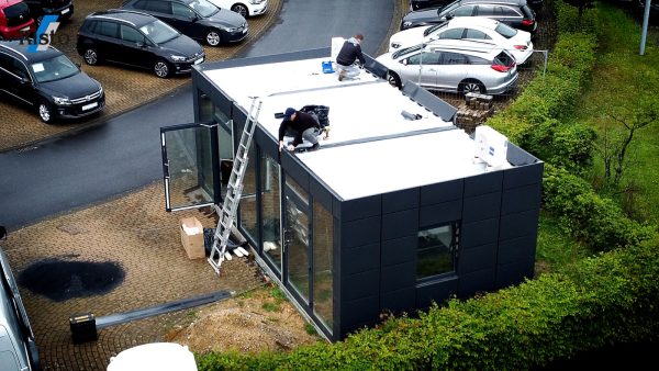 Montage eines Bürocontainers mit Dacharbeiten auf einem Parkplatz