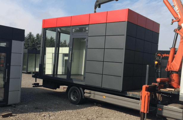 Container wird mithilfe eines Krans vom Tieflader abgeladen – Beispiel für die Anlieferung eines modularen Bürocontainers