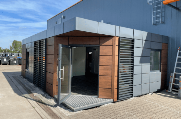 Freistehende Containeranlage mit Fenstersegmenten und moderner Fassadenverkleidung auf Baustellenfläche