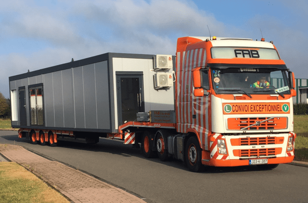Großes Containermodul wird auf einem Spezial-LKW für den europaweiten Transport geliefert