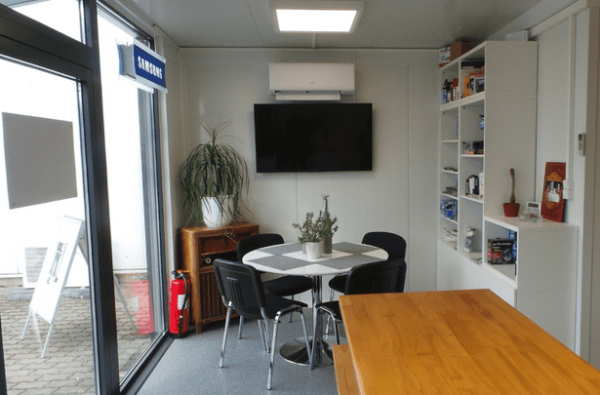 Innenansicht des Bürocontainers mit Besprechungstisch, Wandregal und Klimaanlage